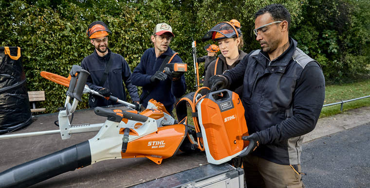Gardeners and landscapers take STIHL AP-System power tools and a backpack battery from their vehicle’s loading area.